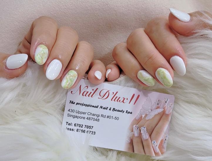 Close-up of hands with elegant white and green marble nails, featuring the Nail D'lux II business card.
