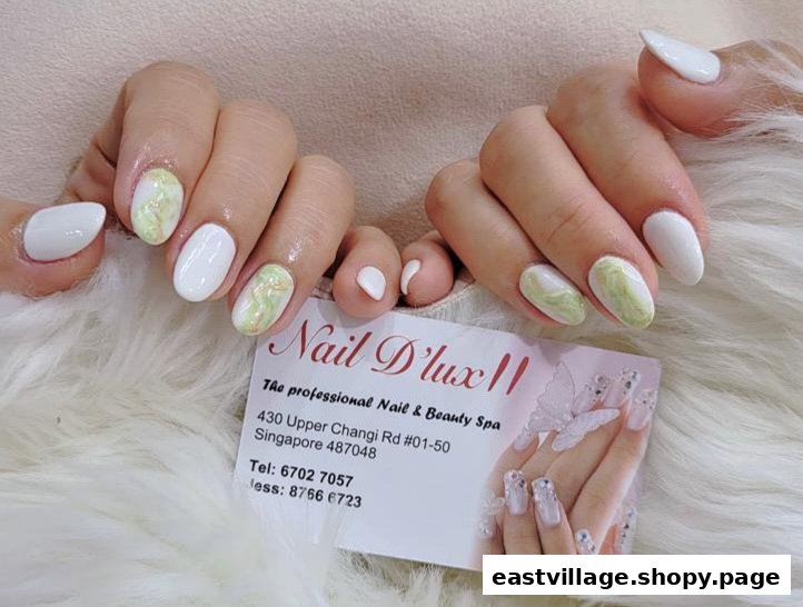 Close-up of hands with elegant white and green marble nails, featuring the Nail D'lux II business card.
