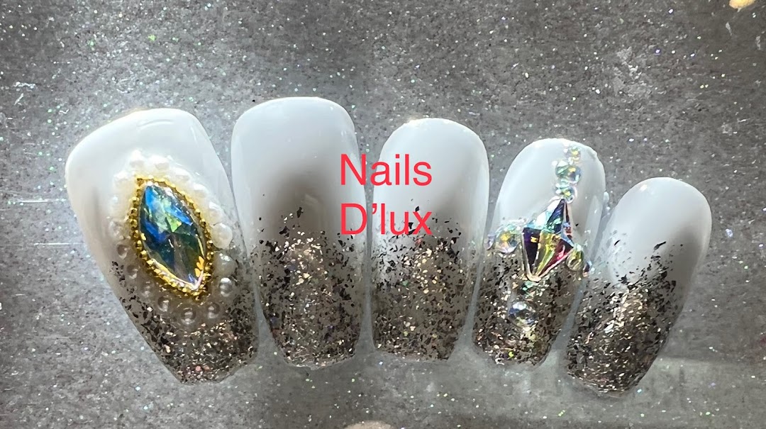 Close-up of five white and glitter nails adorned with sparkling gems and pearls.