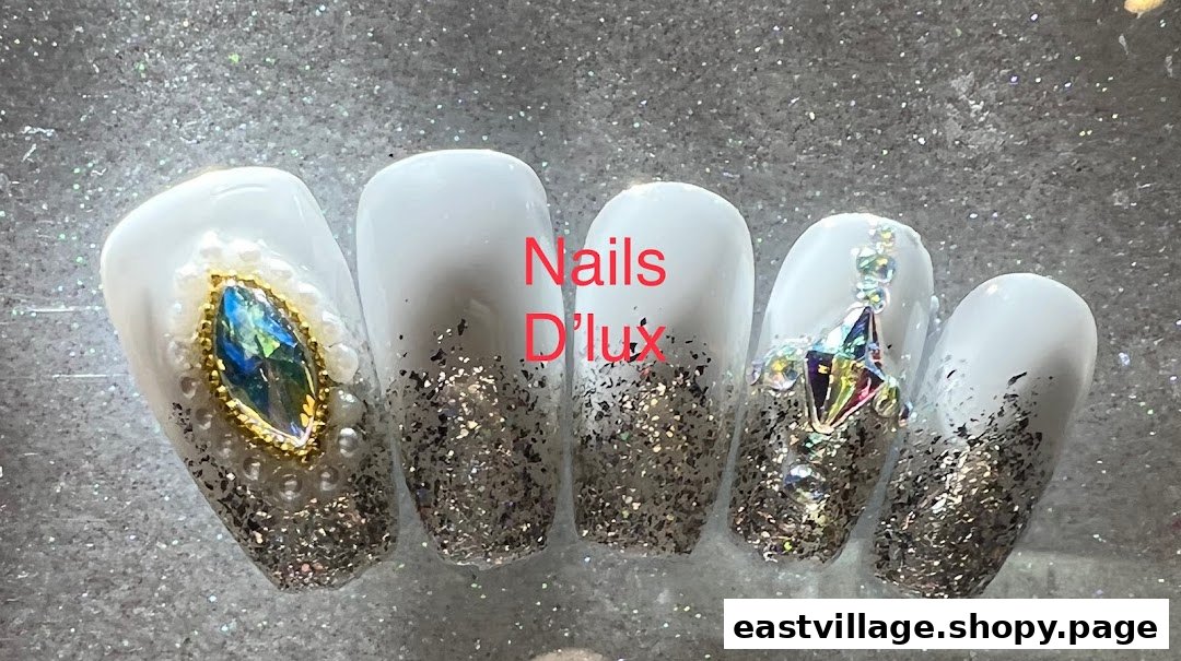 Close-up of five white and glitter nails adorned with sparkling gems and pearls.