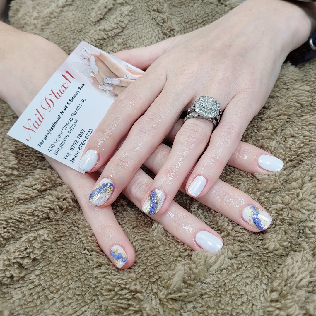 Hands with white and artistic blue/gold manicured nails, holding a Nail D'lux II business card.