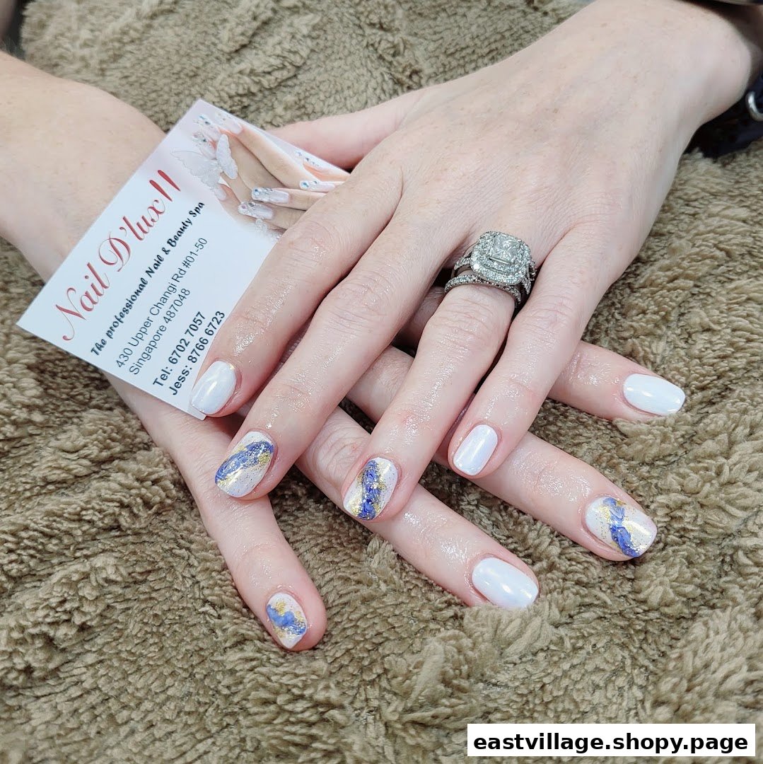 Hands with white and artistic blue/gold manicured nails, holding a Nail D'lux II business card.
