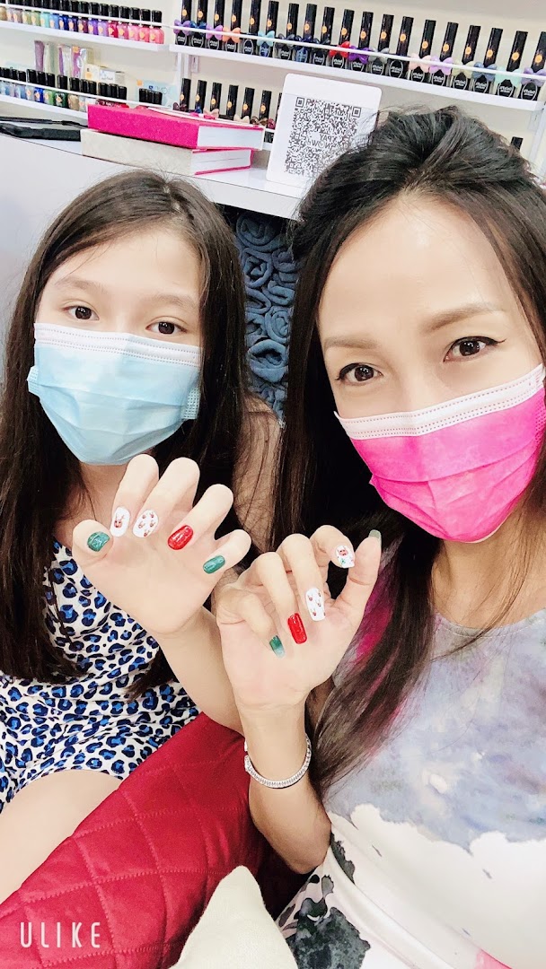 Two masked individuals proudly display their festive, freshly manicured nails inside a nail salon.