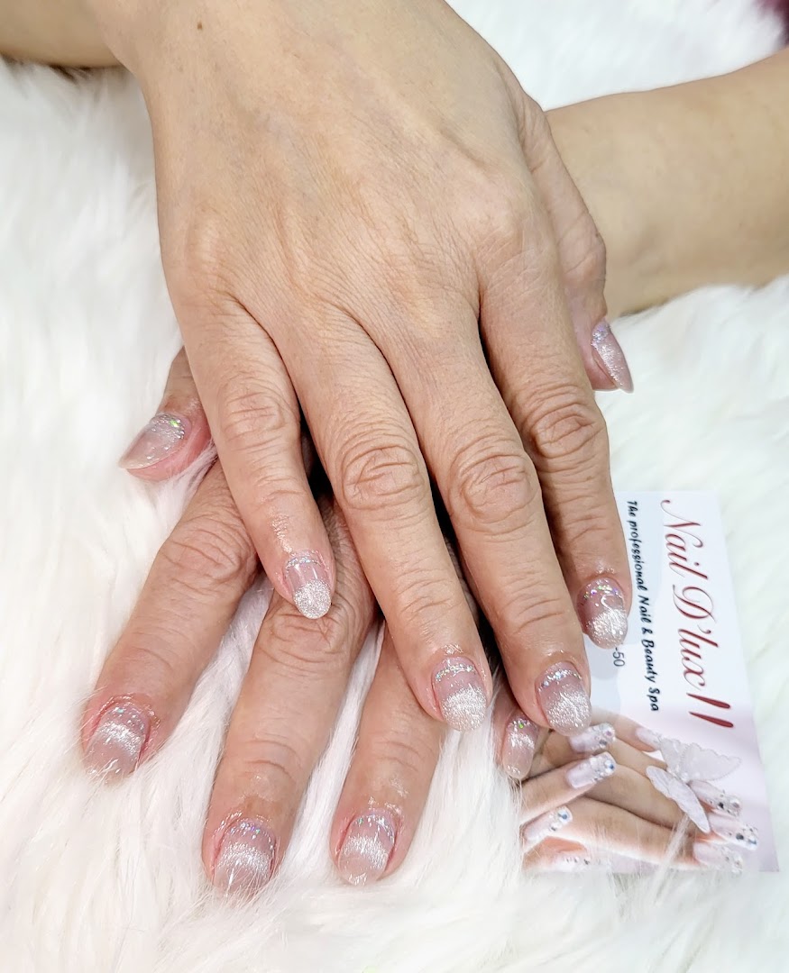 Close-up of hands showcasing sparkling, elegant nail art on a white furry surface, with a Nail D'lux II business card.