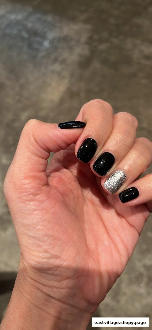 A hand displaying black and silver glitter nail polish, showcasing a finished manicure.