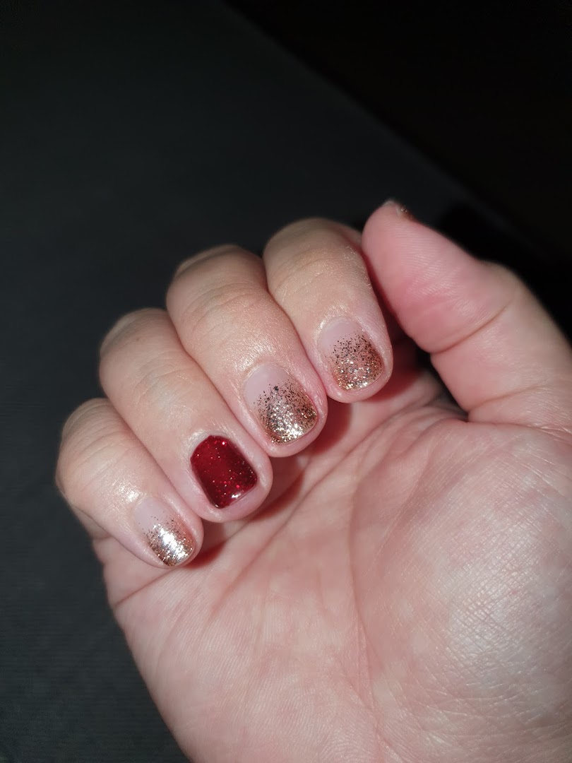 A hand showcasing a festive nail design with red and gold glitter polish.