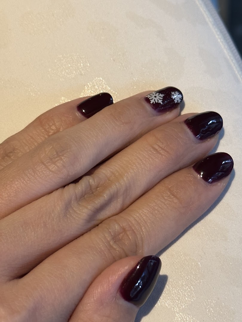 Close-up of a hand showcasing dark red nails with delicate white snowflake art.
