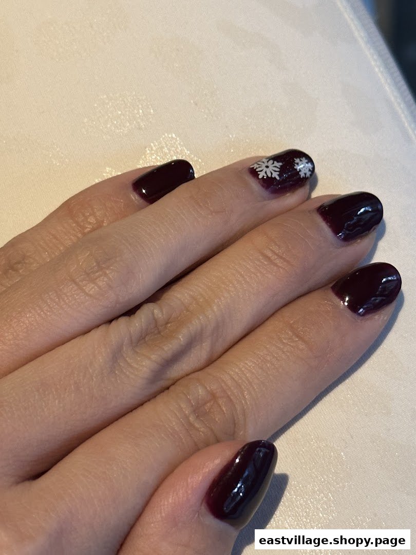 Close-up of a hand showcasing dark red nails with delicate white snowflake art.