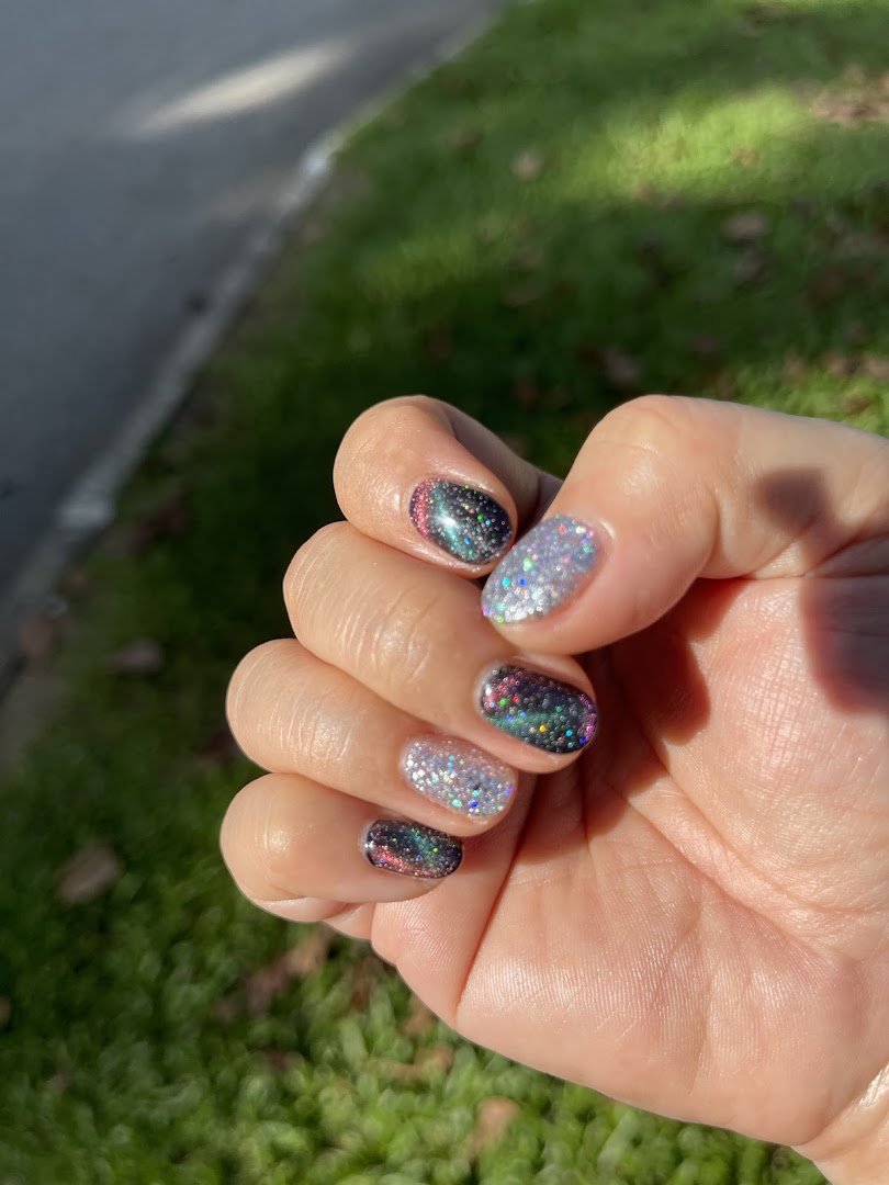 A hand showcasing vibrant, glittery nail polish designs with a mix of dark and light colors.