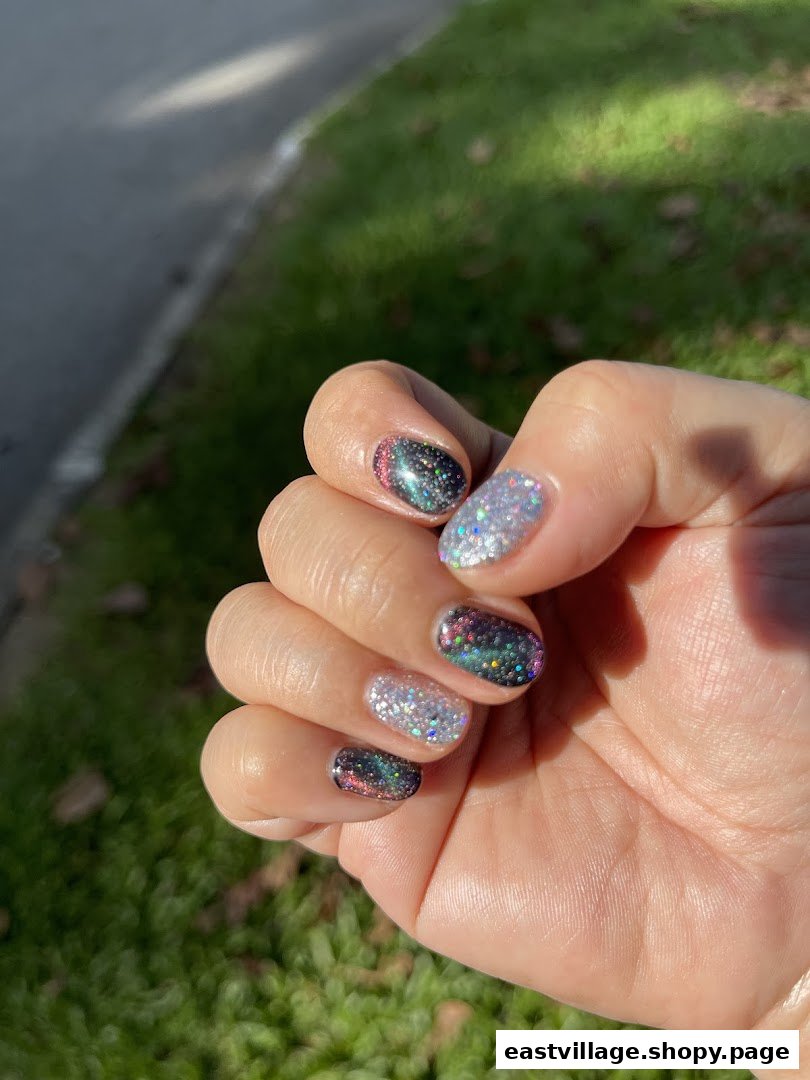 A hand showcasing vibrant, glittery nail polish designs with a mix of dark and light colors.