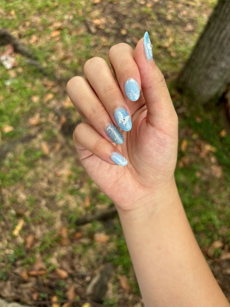 A hand showcasing light blue and glittery nails with intricate butterfly and swirl designs.