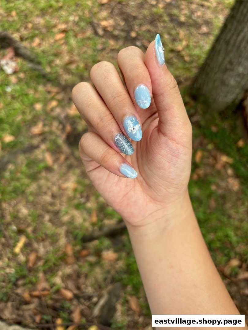 A hand showcasing light blue and glittery nails with intricate butterfly and swirl designs.