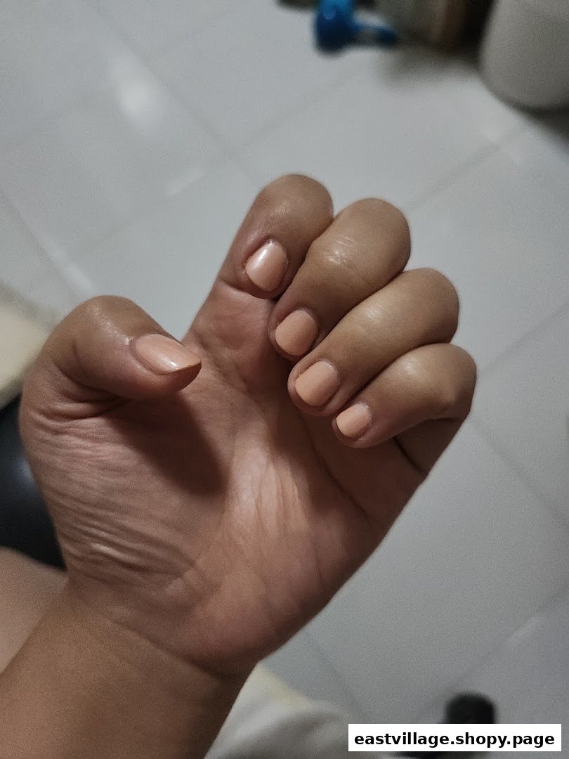 A close-up of a hand showcasing freshly manicured nails with a natural, peachy nude polish.