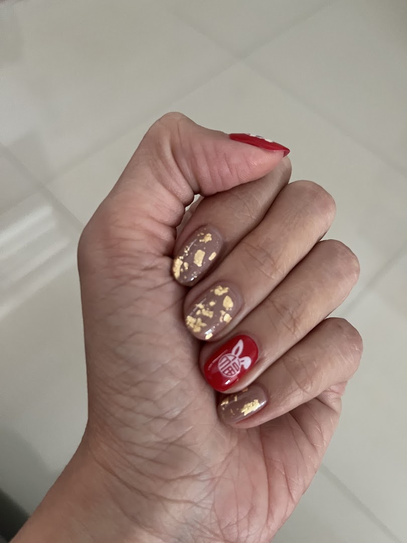 A hand showcasing festive red and beige nail art with gold flakes and a rabbit design.
