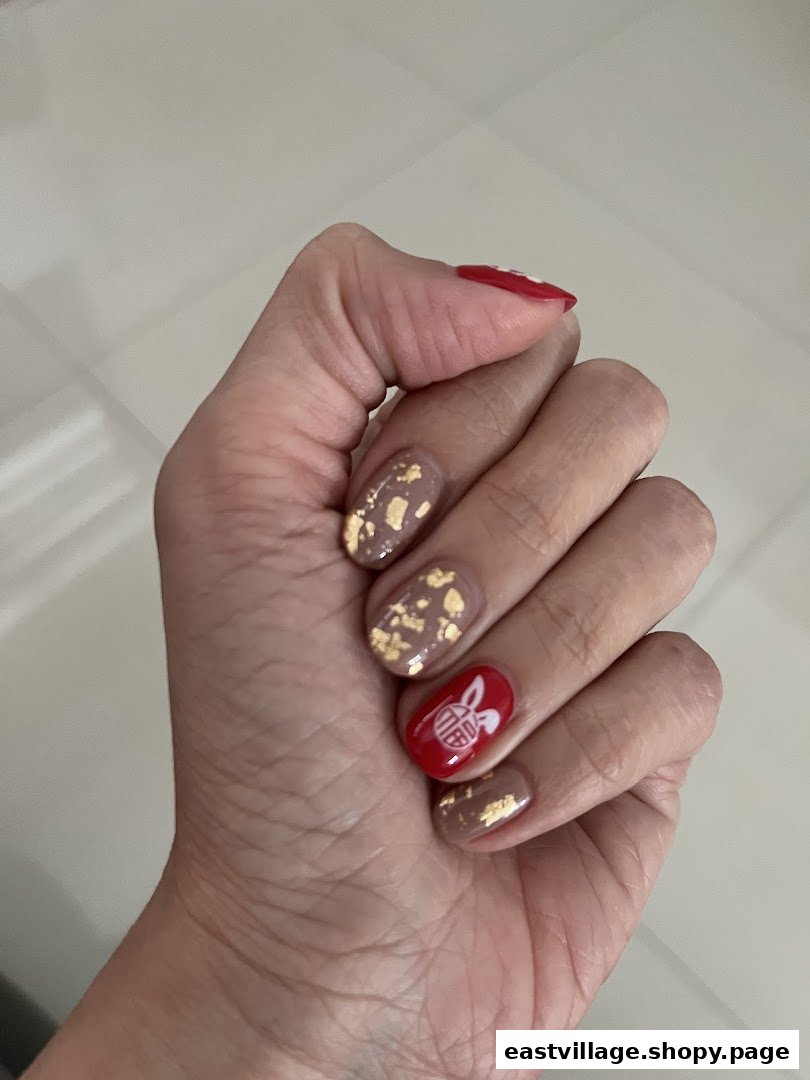 A hand showcasing festive red and beige nail art with gold flakes and a rabbit design.