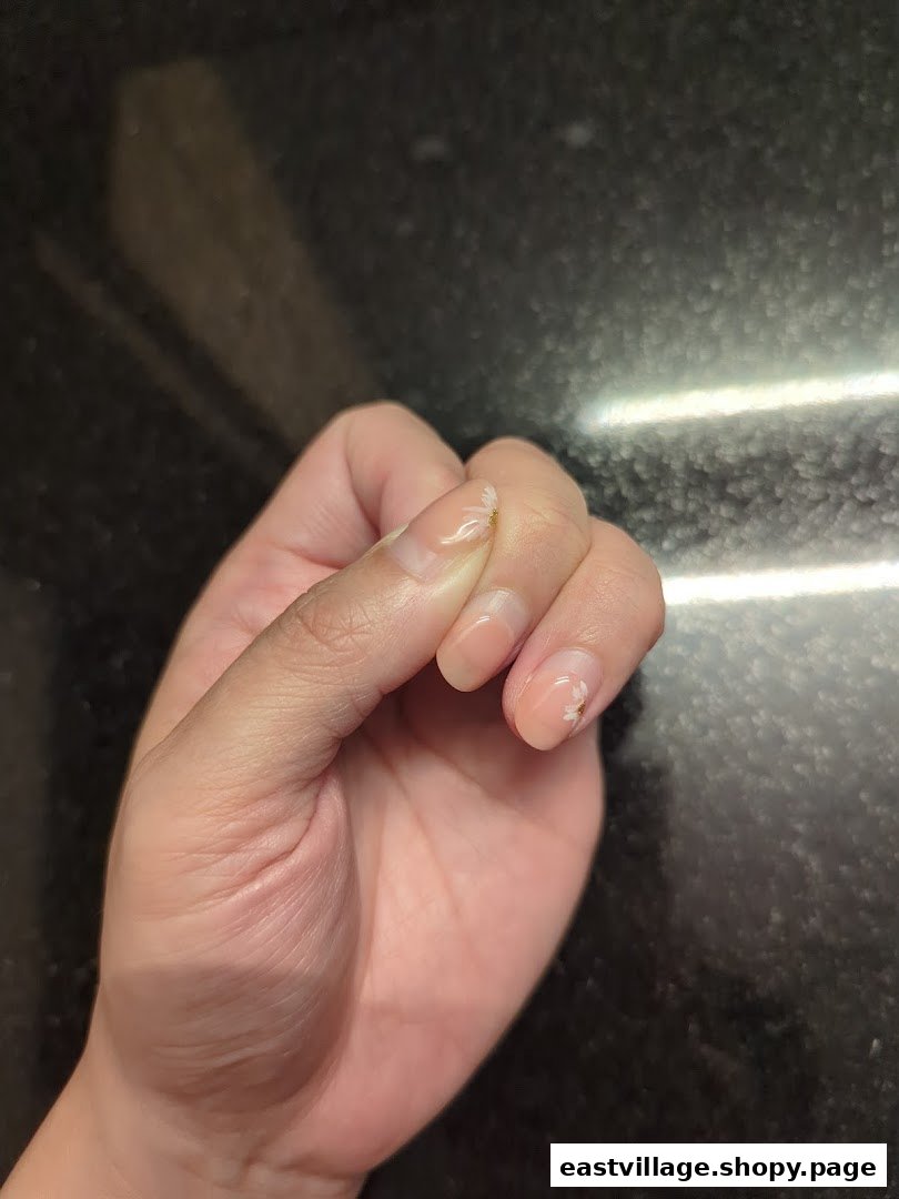 A close-up of a hand displaying delicate nail art with small white floral accents.