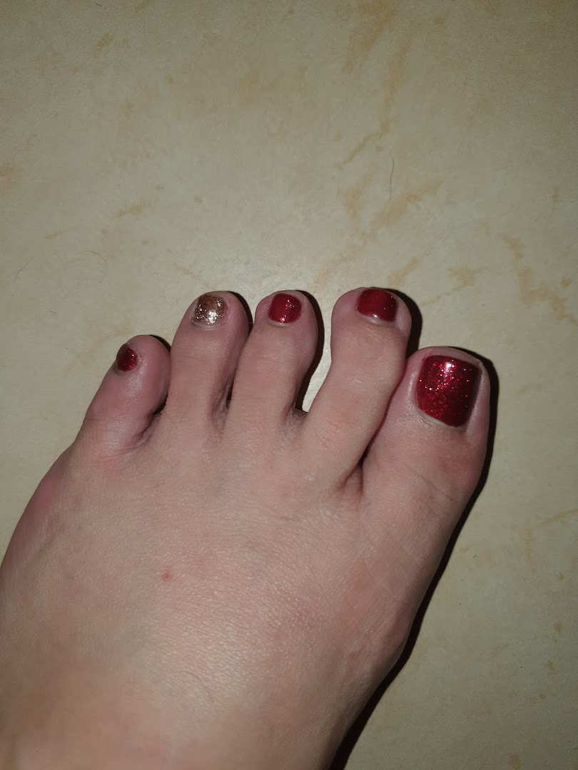 A close-up of a foot showcasing a festive red and gold glitter pedicure.
