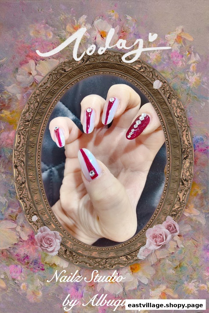 A hand showcasing elegant red and white nail art with rhinestone accents, framed by a decorative mirror.