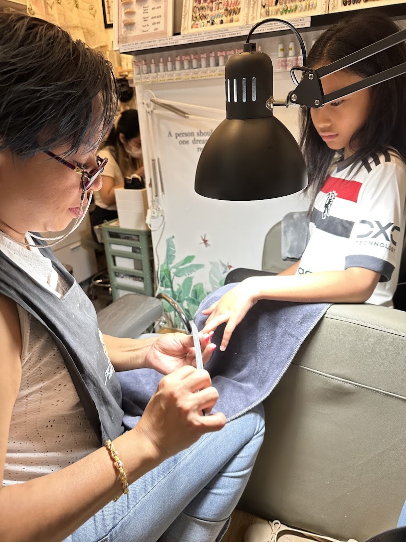 A nail technician meticulously files a young client's nails under a bright lamp in a clean salon environment.