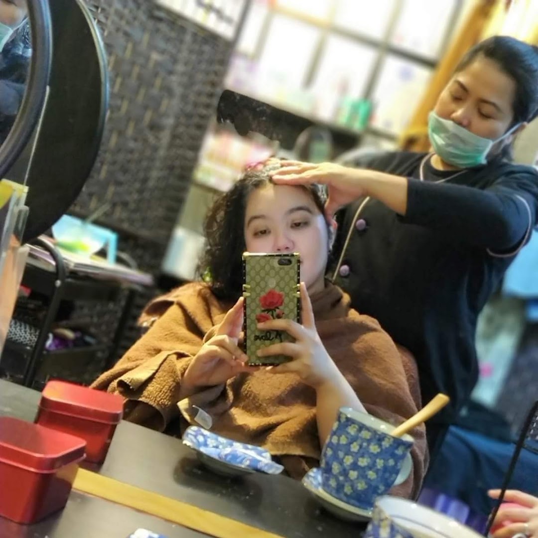 A customer receives a head massage or hair treatment from a masked therapist at Niki Beauty Wellness Salon.