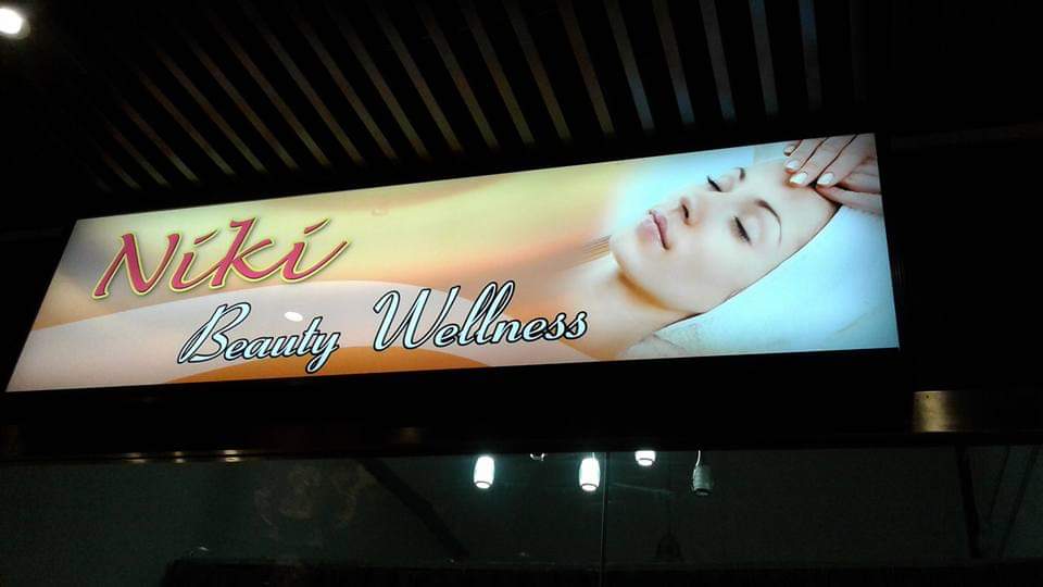 An illuminated sign for Niki Beauty Wellness Salon and Spa, featuring a woman receiving a facial.
