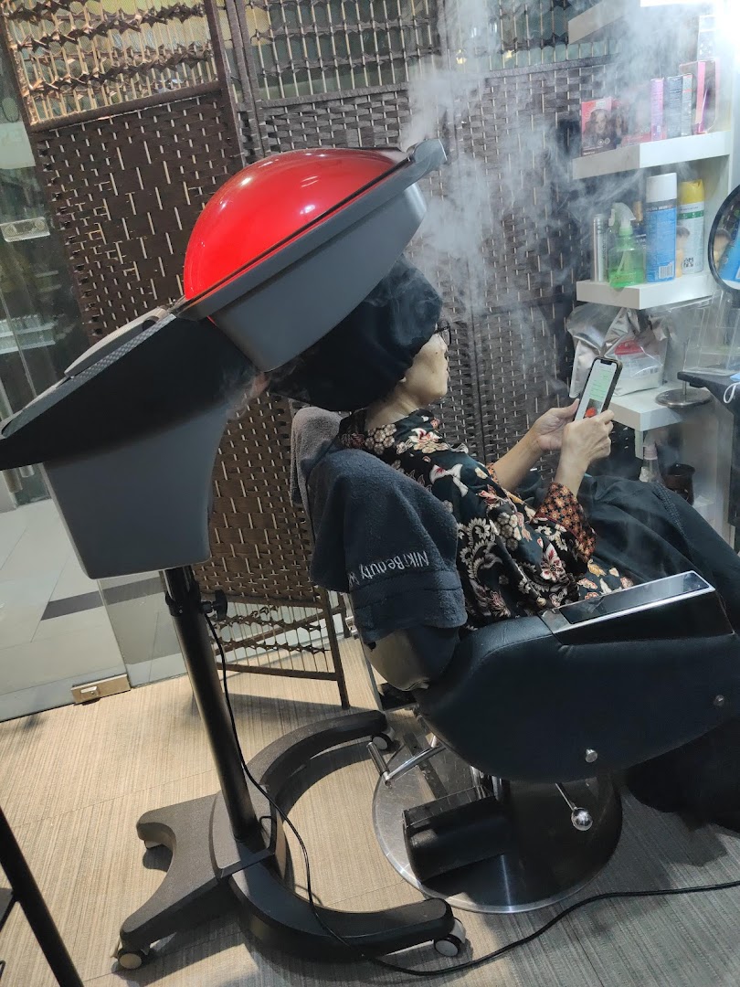 A customer receives a hair steam treatment at Niki Beauty Wellness Salon, relaxing in a salon chair.