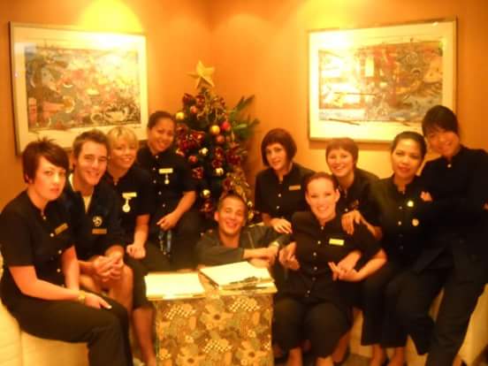 A group of smiling salon staff members gathered around a table with a festive Christmas tree.