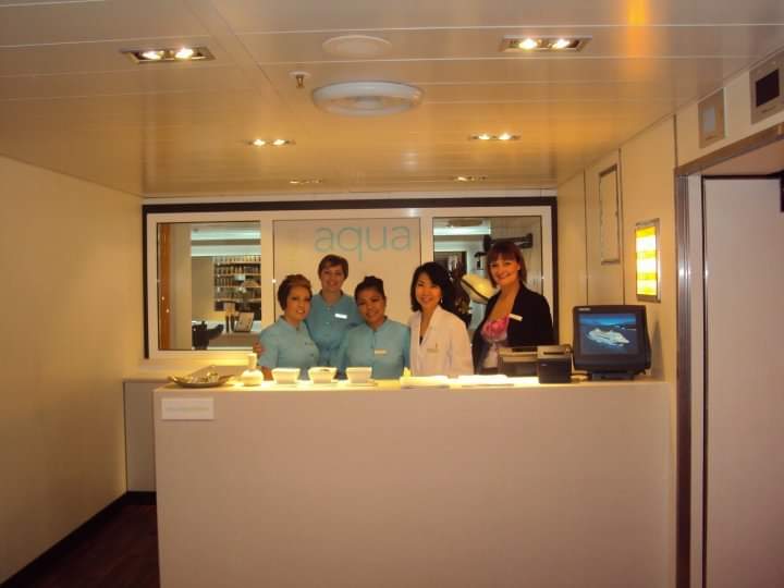 Five friendly staff members at the reception desk of a modern beauty and wellness salon.