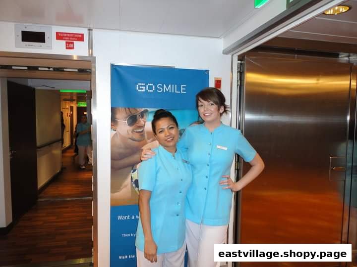 Two salon staff members in light blue uniforms stand beside a 'Go Smile' banner in an interior hallway.