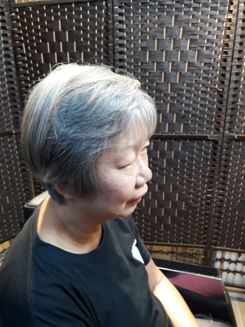 A woman with short, grey hair sitting in a salon chair, with a woven screen in the background.