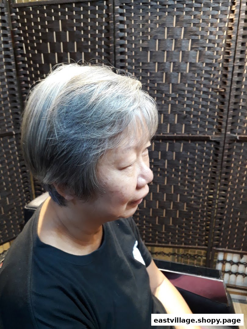 A woman with short, grey hair sitting in a salon chair, with a woven screen in the background.