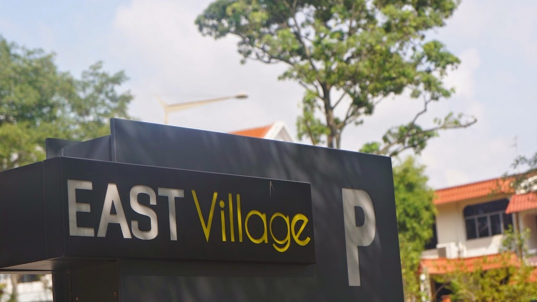 A black sign displaying 'EAST Village' and a 'P' for parking, set against a sky and trees.