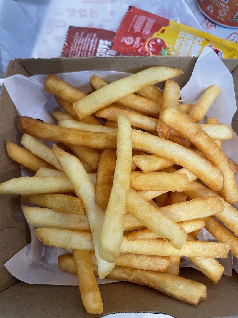 A close-up of a box filled with golden, crispy french fries, accompanied by sauce packets.