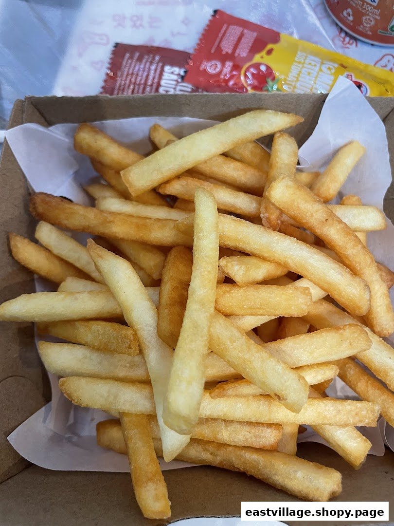 A close-up of a box filled with golden, crispy french fries, accompanied by sauce packets.