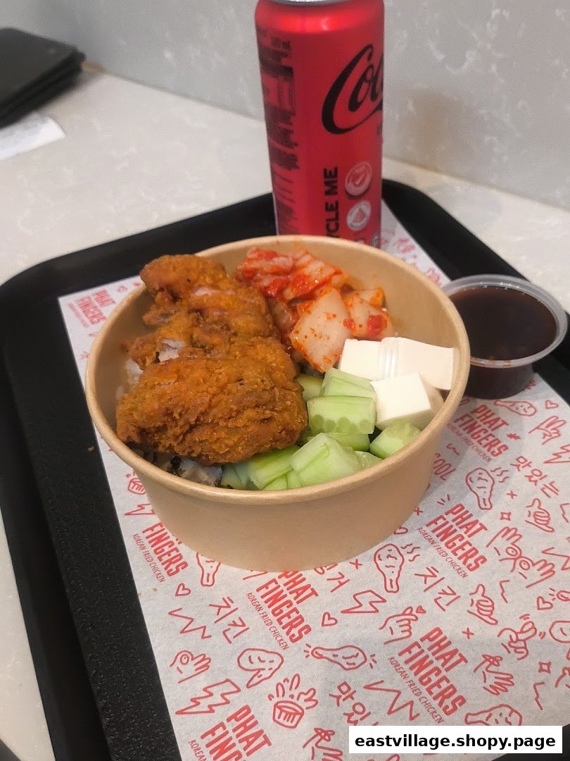 A delicious Korean fried chicken rice bowl with kimchi, cucumber, and a Coca-Cola on a tray.