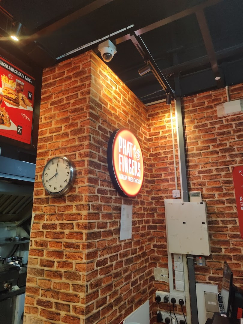 An interior view of Phat Fingers, featuring a brick-patterned wall, a clock, and a branded sign.