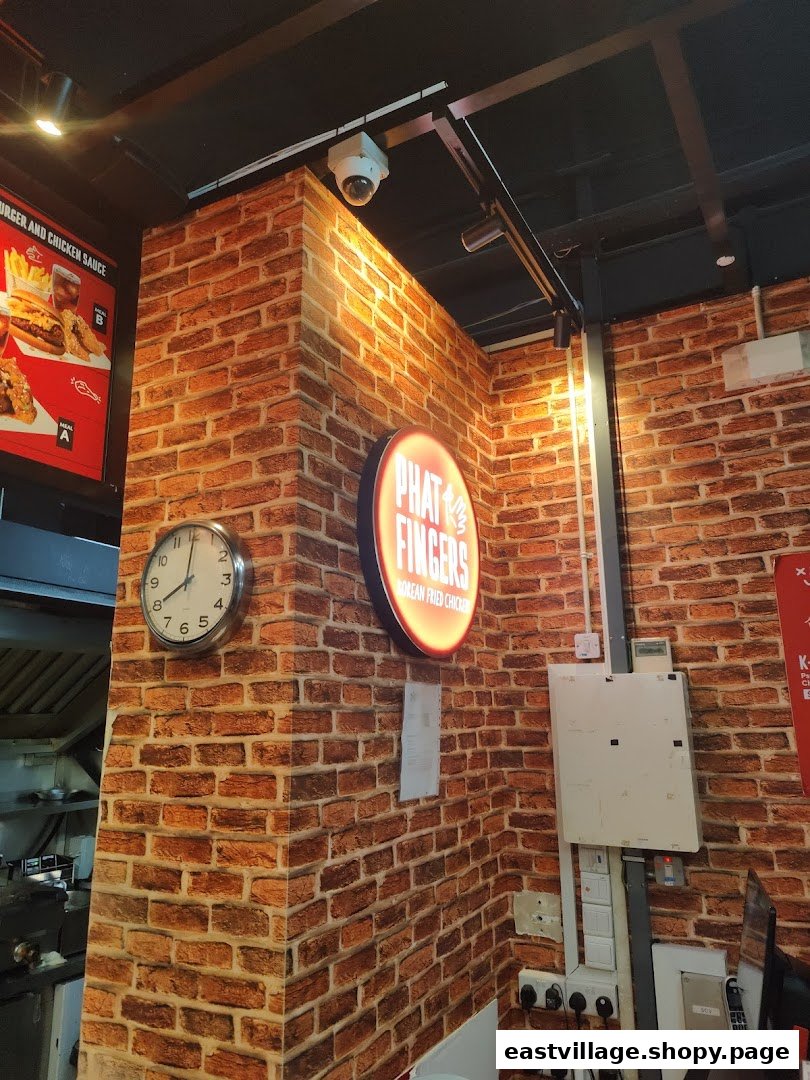 An interior view of Phat Fingers, featuring a brick-patterned wall, a clock, and a branded sign.