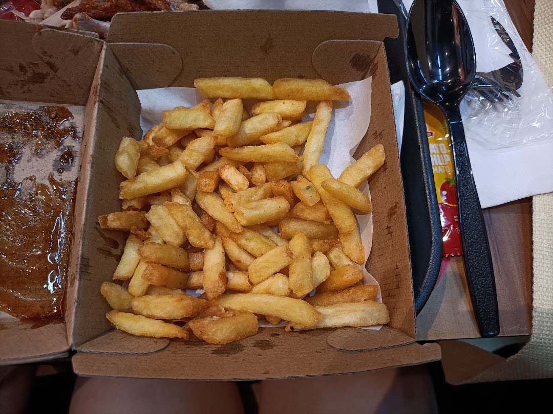 A close-up view of golden french fries in a cardboard box, with a sauce-stained box beside it.