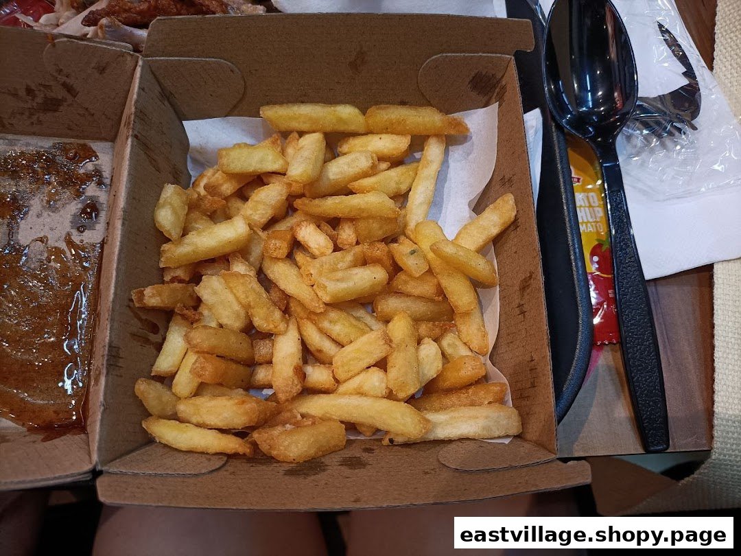 A close-up view of golden french fries in a cardboard box, with a sauce-stained box beside it.