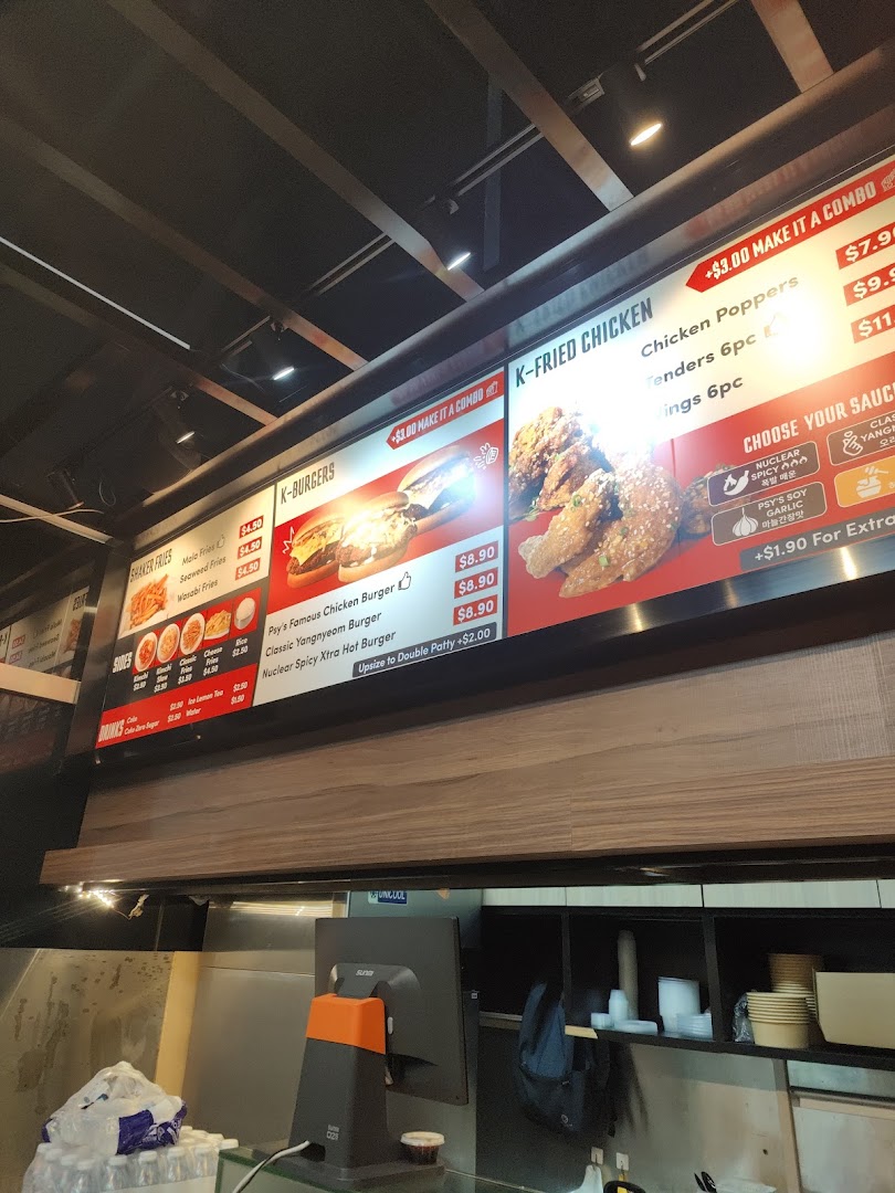A digital menu board displaying Korean fried chicken, burgers, fries, and drink options with prices.