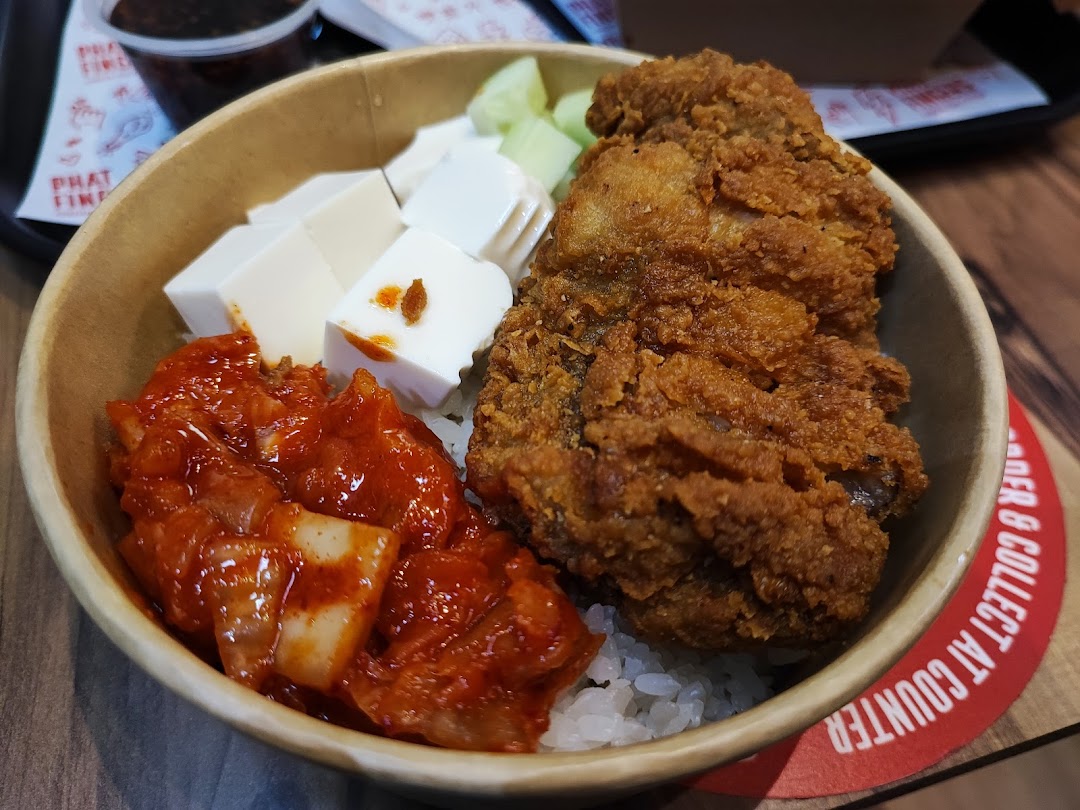 A close-up of a Korean fried chicken rice bowl with kimchi and tofu.