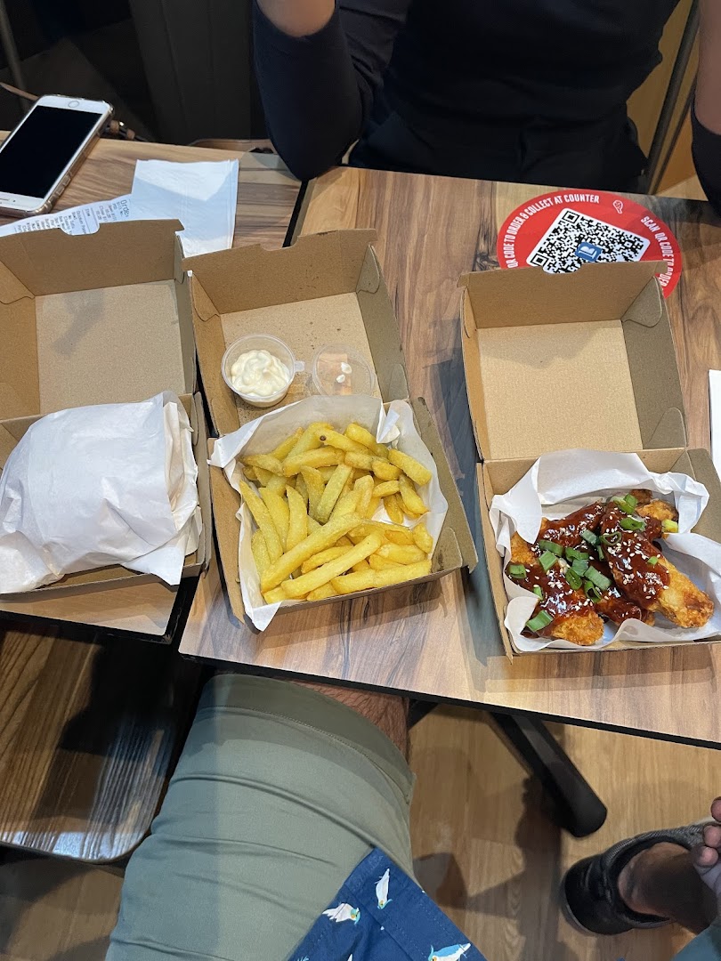 A table with Phat Fingers' Korean fried chicken, crispy fries, and a burger in takeout boxes.