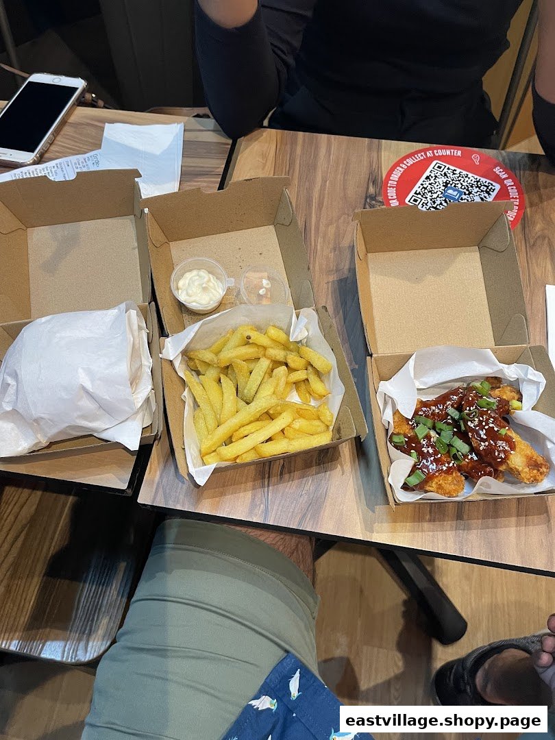 A table with Phat Fingers' Korean fried chicken, crispy fries, and a burger in takeout boxes.