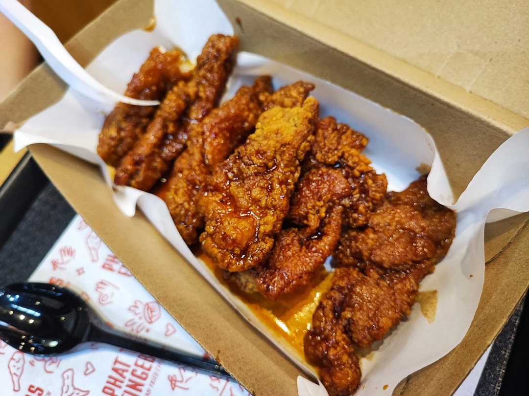 A close-up of crispy, saucy Korean fried chicken tenders served in a brown paper box.