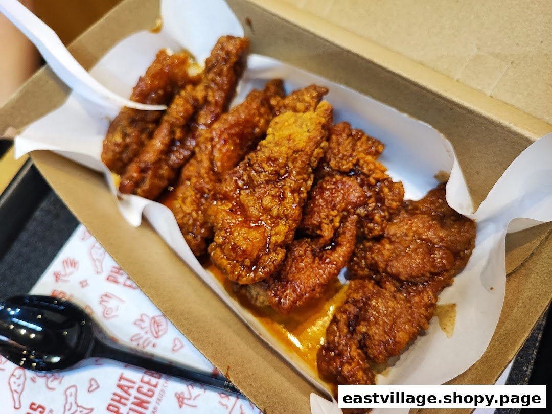 A close-up of crispy, saucy Korean fried chicken tenders served in a brown paper box.