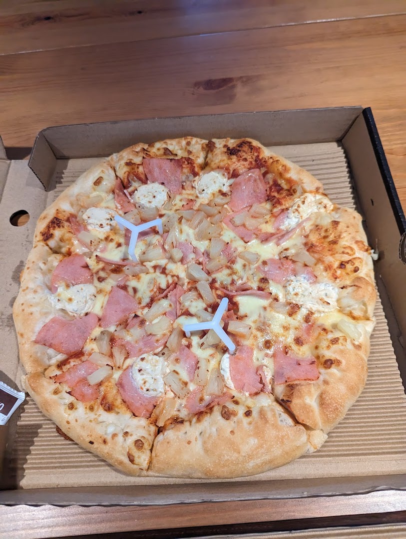 A freshly baked Pizza Hut pizza with ham, pineapple, and cheese in a cardboard box.