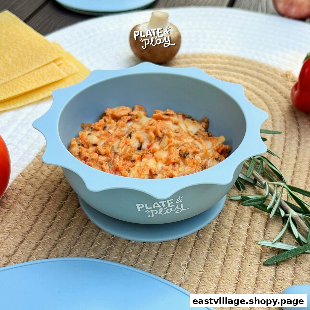 A light blue silicone bowl from Plate & Play filled with food, surrounded by fresh ingredients.