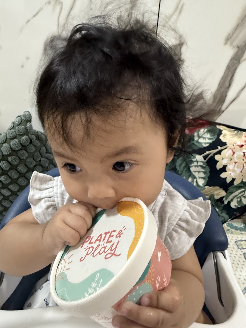 A baby holds a colorful 'Plate & Play' container, engaging with the brand's product.