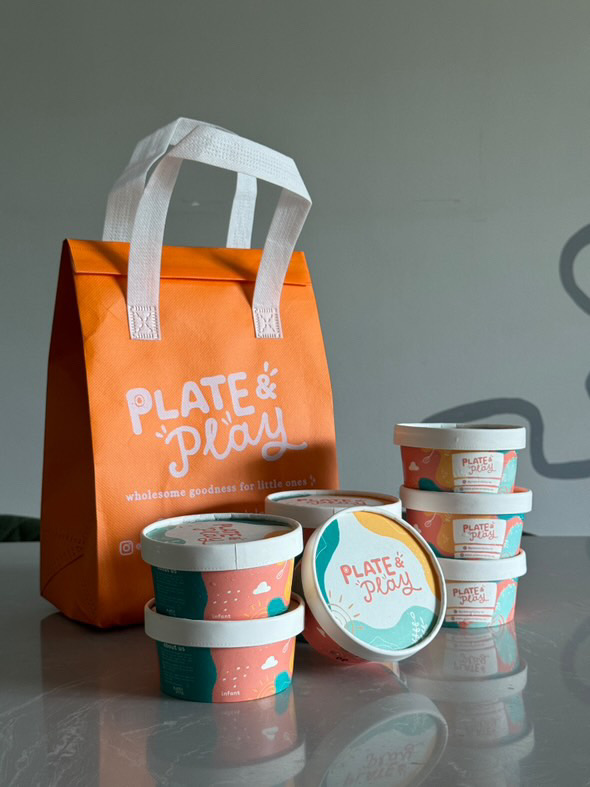Branded orange bag and colorful containers from Plate & Play, offering wholesome goodness for little ones.