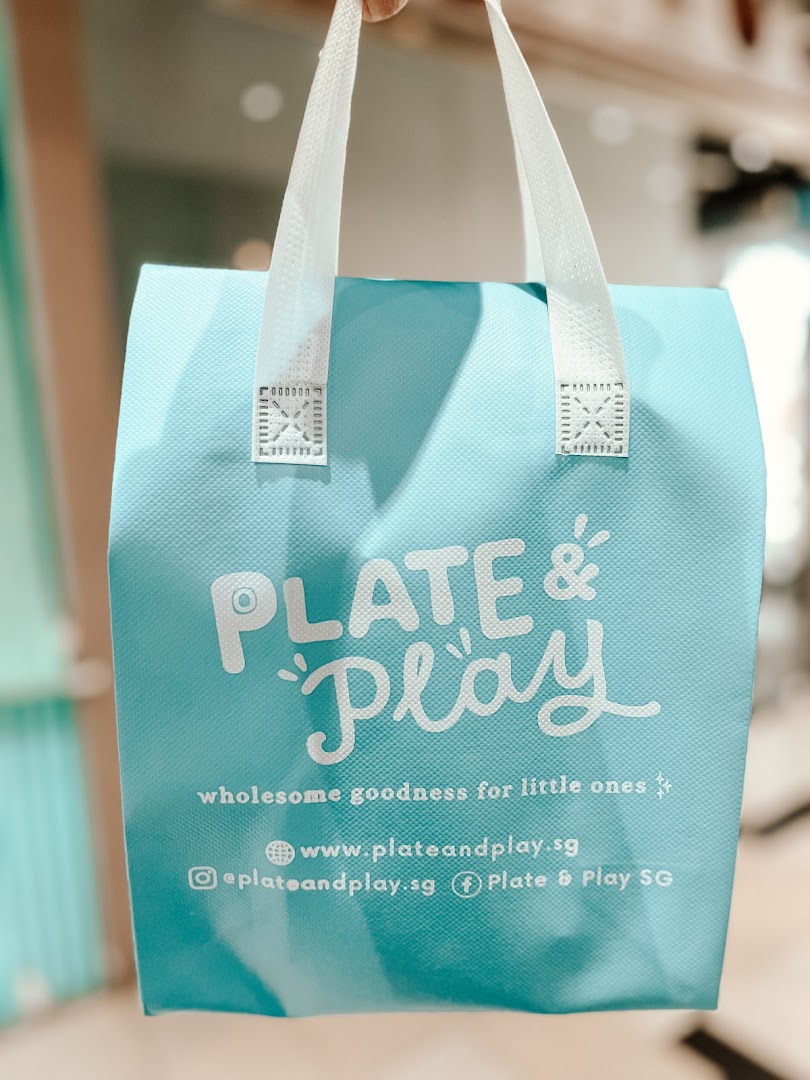 A turquoise shopping bag from Plate & Play, featuring its logo and tagline 'wholesome goodness for little ones'.